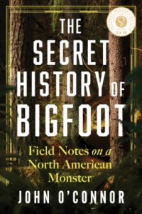 Book cover for The Secret History of Bigfoot by John O’Connor. Image on cover is a gorgeous painting of trees growing in a lush and green woods. They are growing so closely together that the background quickly fades into a dark, leafy place where little sunlight can penetrate the forest floor.