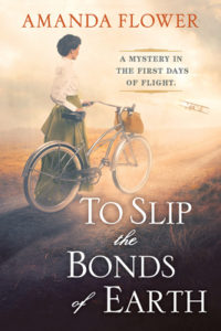 Book cover for To Slip the Bonds of Earth by Amanda Flower. Image on cover shows a painting of a white woman wearing a 1900s-style white blouse and floor length green skirt. She is pushing a bicycle on a dusty country road as her brown satchel hangs from the handle bars. 