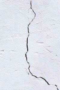 A crack has formed in a white wall. The crack is slender but long. 