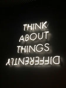 A photo of a white neon sign that says “think about things differently.” The word differently is spelled backwards. This sign has been placed against a black background so it really stands out!