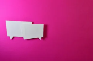 Two square white message balloons pasted overlapping each other onto a hot pink background. 