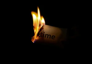 The word time is printed on a piece of cardstock. The cardstock is on fire and the flames have almost reached the printed word on this document. 