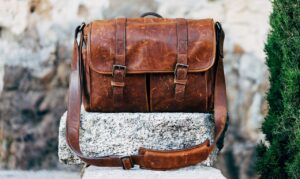 A vintage brown leather bag sitting on a white rock carved into the shape of what appears to be a low fence.