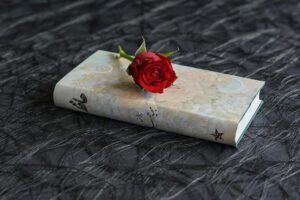 A hardback, cream-coloured book of Persian poetry that has a single red rose lying on the book.