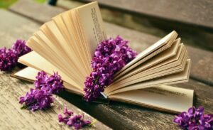 Several bunches of lilacs lying on or next to an opened hardback book that’s laying on a wooden porch or bench. 