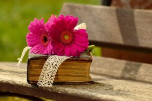 Two pink gerbera flowers are lying on an antique hardcover book that’s also been wrapped in a white lace ribbon.