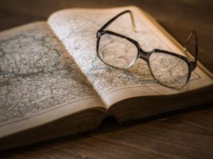 A pair of glasses, possibly reading glasses, lying on a page of an opened book that has a map drawn on it. 
