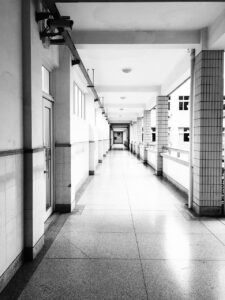 Black and white photo of an empty hallway filled with sunlight in a school. 