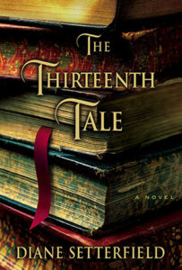 Book cover for The Thirteenth Tale by Diane Setterfield. Image on cover shows a drawing of three hardback novels neatly stacked in a small pile together. One of the books has a red cloth book cover that is hanging out between its pages and draping down to the wooden surface below. 