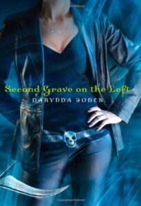 Book cover for Second Grave on the Left (Charley Davidson, #2) by Darynda Jones. Image on cover shows a realistic painting, or maybe a heavily photoshopped photo, of a young white woman who has one hand on her hip and is wearing jeans, a jacket, and a blouse that shows a hint of cleavage. 
