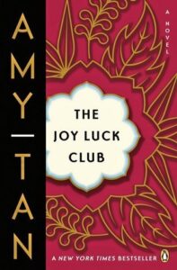 Book cover for The Joy Luck Club by Amy Tan. Image on cover shows golden metal leaves and flowers arranged in a beautiful circular pattern against a dark pink background. 