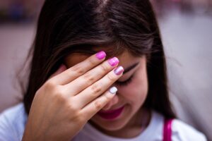 Young brown girl holding her hand over her forehead in embarrassment. Her nails are painted various shades of pink. 