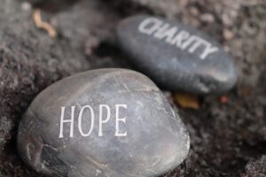 Grey stones in a stone garden. The stone closest to the viewer has the word “hope etched onto it. The stone right behind it has the world “charity” etched onto it. 