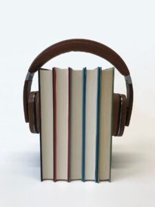 Five hardcover books standing up on a white surface. They are held upright and together in place by a pair of earphones that are wrapped around them in the same way you’d see a person wear earphones. 