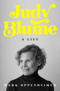 Book cover for Judy Blume: A Life by Mark Oppenheimer. Image on cover is a photo of Judy Blume with short curly hair and in a black turtleneck sweater. She’s smiling faintly and looking off to her left. 