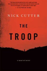 Book cover for The Troop by Nick Cutter. image on cover shows the silhouette of someone standing on top of a hill against a reddish-orange sky, probably just after dusk or just before dawn given how heavy the shadows are. 