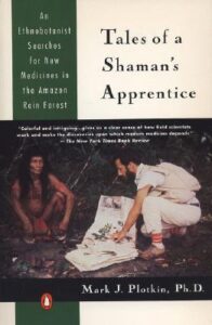 Book cover for Tales of a Shaman's Apprentice: An Ethnobotanist Searches for New Medicines in the Rain Forest by Mark J. Plotkin. Image on cover shows a white man wearing an all white outfit crouching next to a South American Native person who is talking to him about, presumably, medicinal plants in the rainforest. 