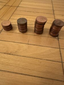 Closeup shot of four stacks of various amounts of pennies on a wooden floor. 