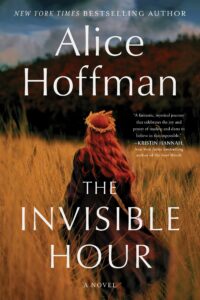 Book cover for The Invisible Hour by Alice Hoffman. Image on cover shows a young white woman with wavy red hair walking away from the viewer in a golden grassy field. She has a small wreath of flowers on her head  and is wearing a dark cloak. 