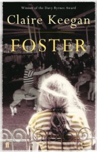 Book cover for Foster by Claire Keegan. Image on cover shows a blurry image of a young white girl sitting as she watches other children ride a merry-go-round. 