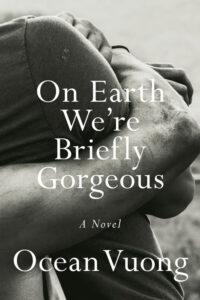 Book cover for On Earth We're Briefly Gorgeous by Ocean Vuong. Image on cover is a black and white shot of a pair of muscular arms wrapped around a man’s knees as he sits on the ground. 