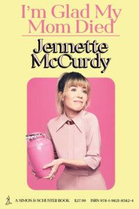 Book cover for I'm Glad My Mom Died by Jennette McCurdy. Image on cover shows the author wearing a light pink dress and smiling uncomfortably as she holds a dark pink oblong object.