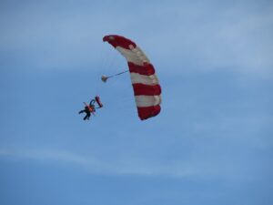 A sky diver floating gracefully through the air on a nearly cloudless day. Their red and white striped parachute has just opened. 
