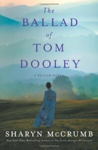 Book cover for The Ballad of Tom Dooley (Ballad, #9) by Sharyn McCrumb. Image on cover is a painting of a woman in a long, blue, 1800s-style dress walking alone on a windy and foggy plain. There are mountains in the distance.