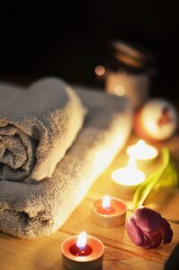 White towels folded up and stacked together. Lit tea light candles and a rose beside them. This sets the scene for a nice massage! 