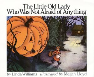 Book cover for The Little Old Lady Who Was Not Afraid of Anything by Linda Williams. Image on cover shows a jack-o-lantern sitting by the side of a road as an old woman begins walking on that road. At the end of the road is a small house whose windows are illuminated with light as dusk approaches. 
