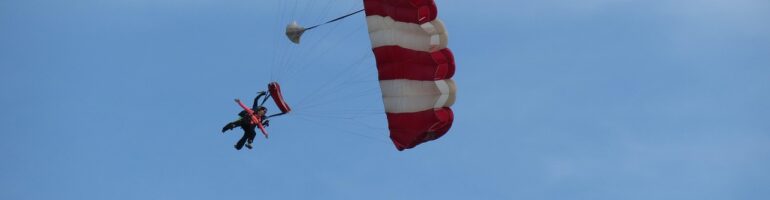 A sky diver floating gracefully through the air on a nearly cloudless day. Their red and white striped parachute has just opened.